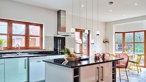Een moderne keuken met een centraal kookeiland, een eethoek met een gele stoel en grote ramen.