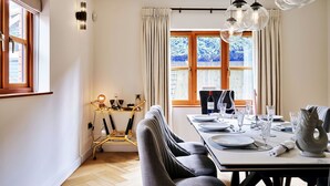 Een eethoek met een gedekte tafel voor twee personen, een bank en uitzicht op een besneeerd landschap door grote ramen.