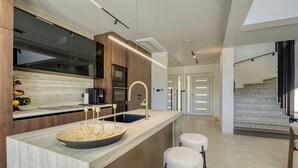 A modern kitchen with a central island, bar stools, and a staircase leading to another level.
