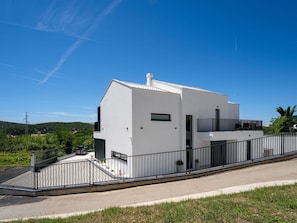 Ein modernes, weißes Gebäude mit Balkon, befestigter Auffahrt und einem Metallzaun.