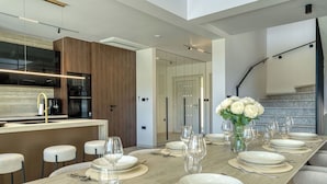 A modern kitchen with a long dining table set for six, a built-in oven, and a staircase leading to an upper level.