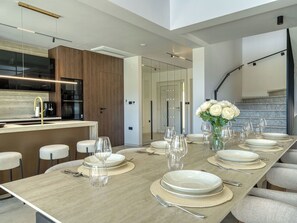 Une cuisine moderne avec une longue table à manger pouvant accueillir six personnes, un four encastré et un escalier menant à un niveau supérieur.