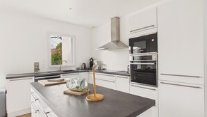 Une cuisine moderne avec des meubles blancs, un grand îlot central doté d’un saladier en verre et un four Bosch.
