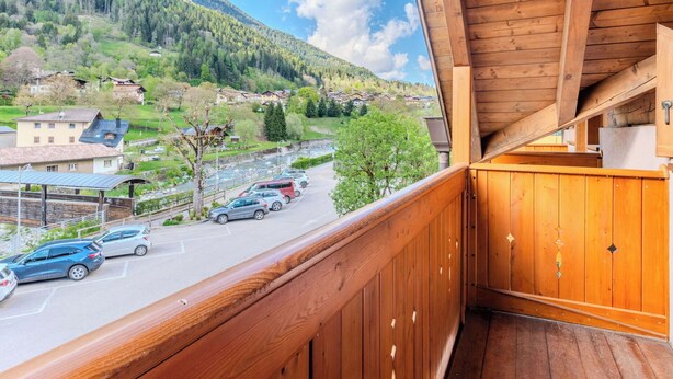 Un balcon en bois offrant une vue sur une montagne, un parking et des bâtiments situés dans la vallée.