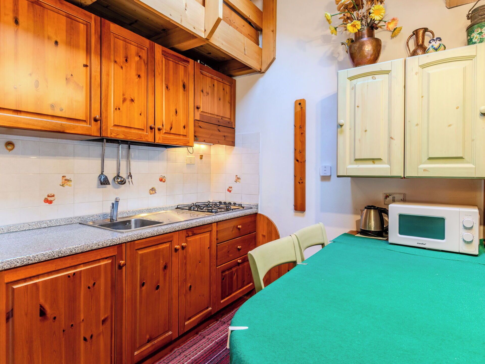 Una cocina con armarios de madera, una estufa a gas, un fregadero, un microondas y una mesa con mantel verde.