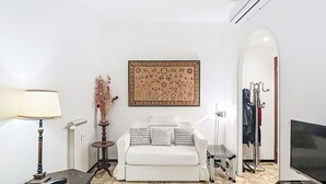 A living room with a white sofa, a lamp, a decorative vase, a framed artwork, a coat rack, and a television. - Beautiful apartment for 4 guests with A/C, WIFI, TV and terrace (Santa Margherita Ligure)