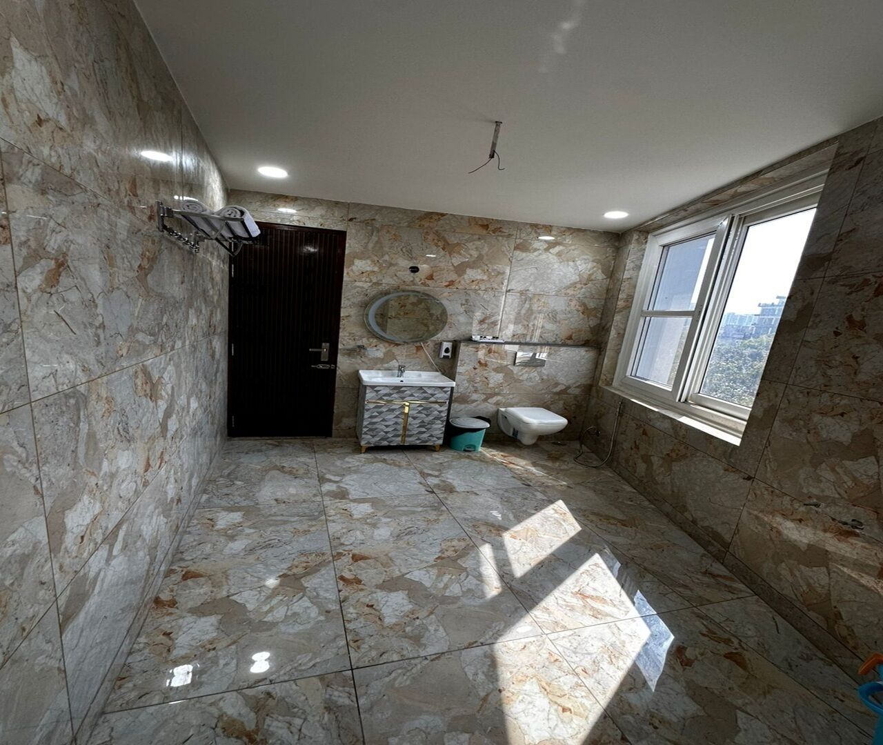 Un baño con paredes y suelo de mármol, un lavamanos, inodoro y una ventana con vistas.