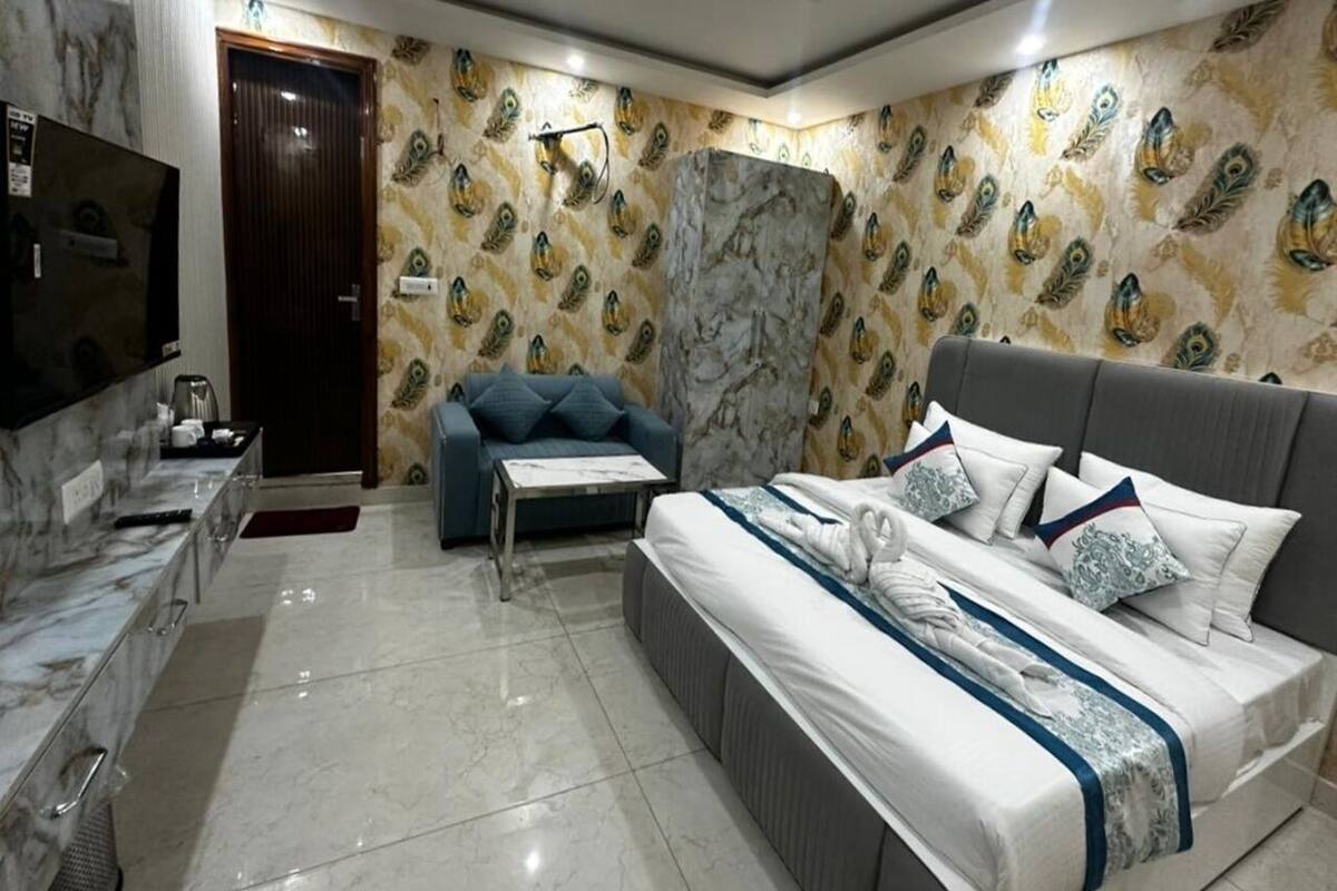 Une chambre d’hôtel moderne avec un meuble-lavabo en marbre, un lit avec du linge de maison blanc et des coussins décoratifs, un canapé bleu et un papier peint à motifs de paon.