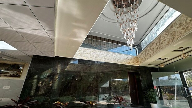 A modern lobby with a large marble reception desk, a chandelier, and potted plants.