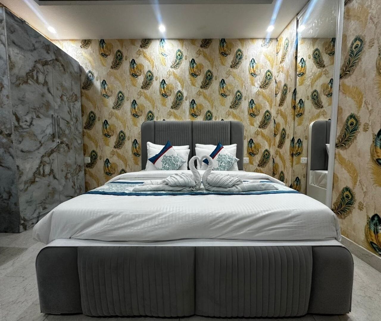 Quarto de hotel moderno com uma cama grande, parede de mármore e papel de parede com padrão de pavão.