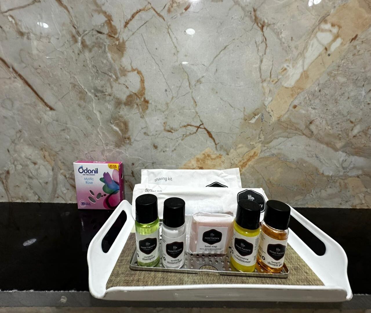 A tray with various toiletries including a shaving kit, a box of Odonil Mystic Rose, and bottles of hotel soap and shower gel.