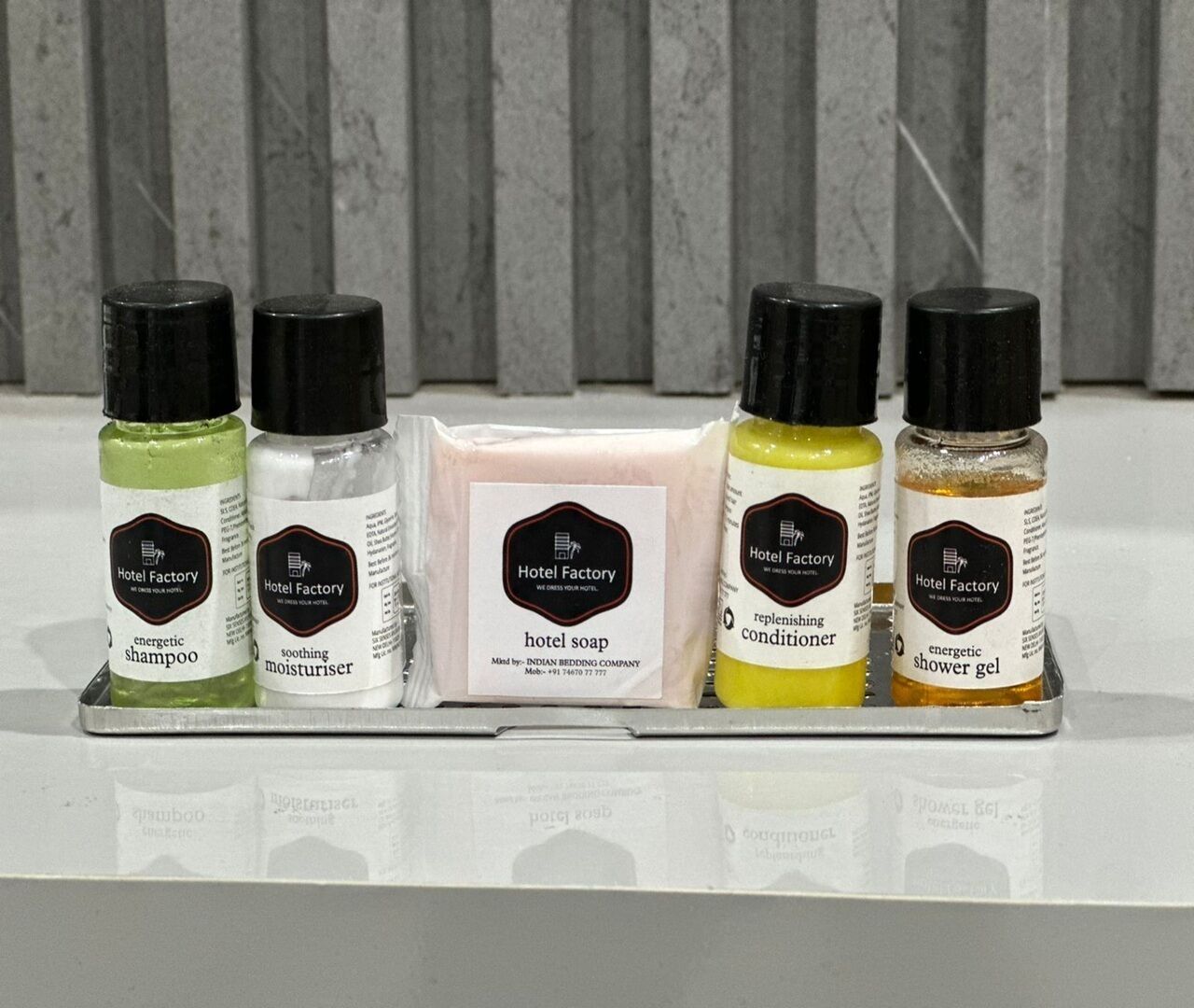 A display of Hotel Factory products including energizing shampoo, soothing moisturizer, hotel soap, replenishing conditioner, and shower gel.