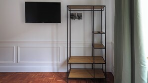 Une pièce dotée d’un parquet en bois disposé en motif «point de Hongrie», d’un téléviseur noir fixé au mur et d’une étagère en métal noir avec des étagères en bois.