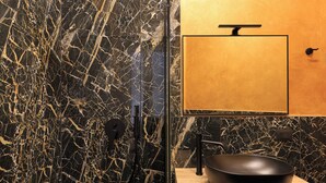 Une salle de bain avec un mur en marbre noir, un meuble-lavabo en bois, un lavabo noir et un miroir avec un cadre doré.
