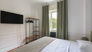 Une chambre à coucher avec un lit, un téléviseur fixé au mur, un radiateur et une fenêtre avec des rideaux.