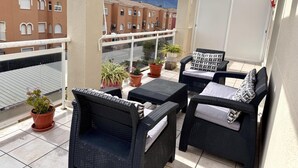 En balkon med fletningsmøbler, plantekasser og udsigt til bygninger og bjerge.