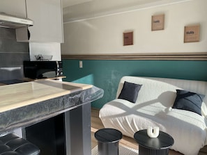 Eine moderne Küche mit einer Holzarbeitsplatte, einem schwarzen Stuhl und einer Mikrowelle. Es gibt ein weißes Sofa mit zwei Kissen und einen kleinen runden Tisch mit einer Kerze.