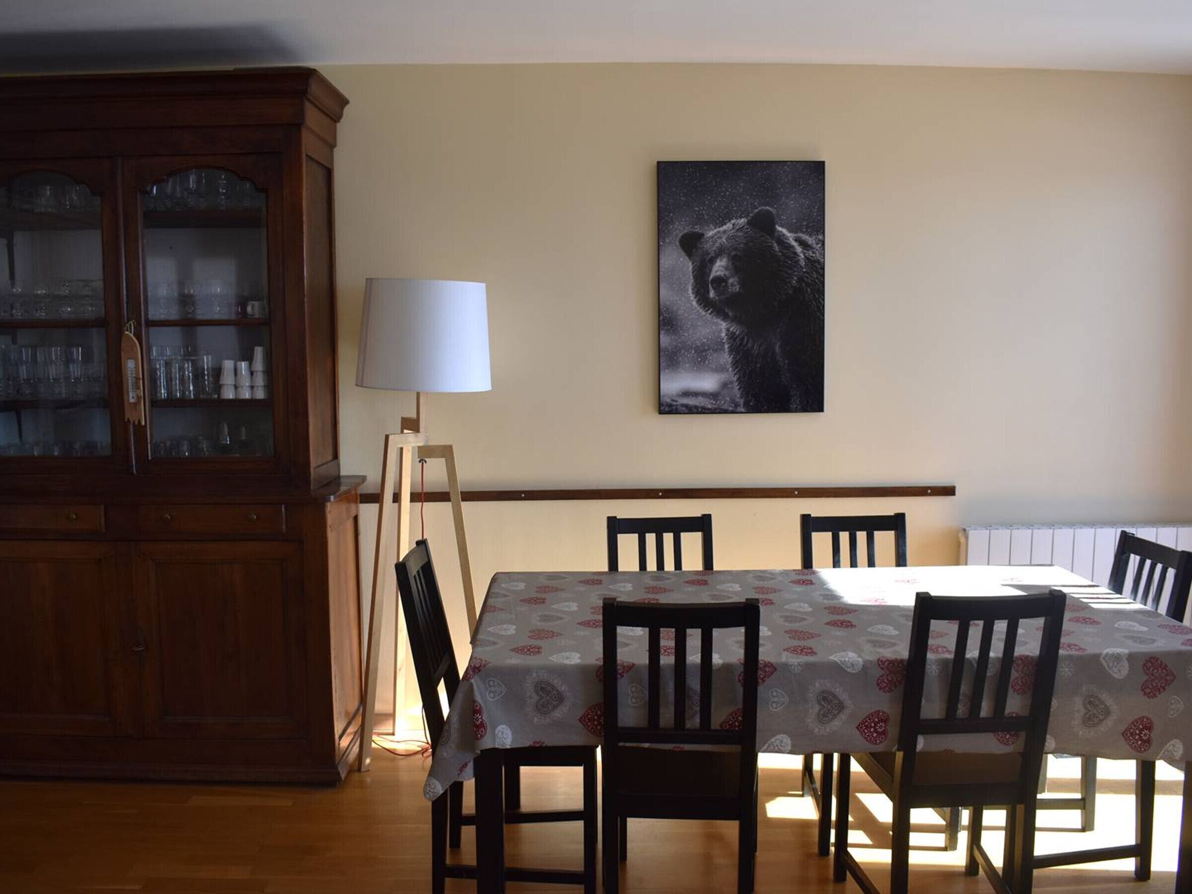 A dining area with a table set for four, surrounded by chairs, a cabinet with glass doors, and a wall-mounted lamp.