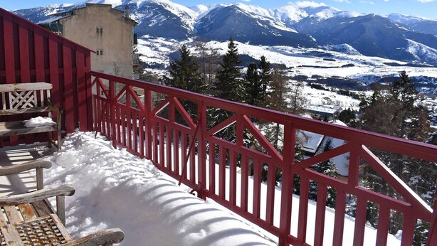 Un balcon avec une balustrade rouge donnant sur un paysage montagneux enneigé.