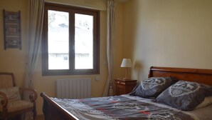 Une chambre à coucher avec un lit en bois, une chaise, une table de chevet avec une lampe et une fenêtre avec des rideaux.