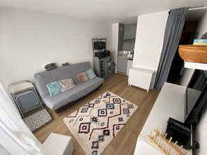 A compact living space with a grey sofa, a patterned rug, and a kitchenette in the background. - Studio with balcony, free parking, near slopes (Arette)