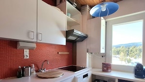 A compact kitchen with white cabinets, a red tiled backsplash, a built-in stove, and a window with a view of trees. - Cozy T2 Cabin with enclosed loggia (Bolquère-Pyrénées 2000)