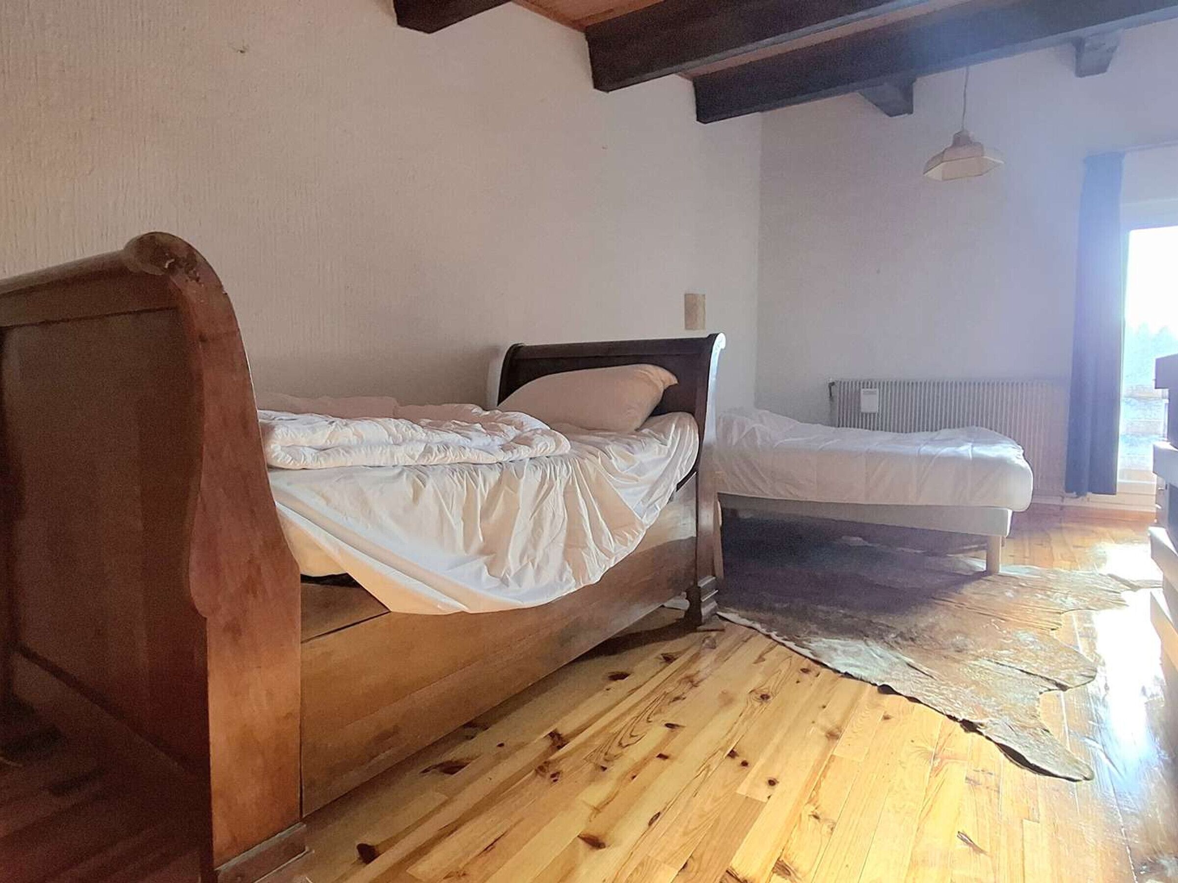 Quarto com duas camas de madeira, um radiador e um lustre.