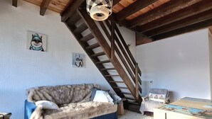 A cozy living room with a blue sofa, a wooden staircase, and two wall-mounted pictures. - Cozy T2 Cabin with enclosed loggia (Bolquère-Pyrénées 2000)