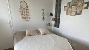 Ett sovrum med en säng, kuddar, en drömfångare, en lampa och inramade bilder på väggen.