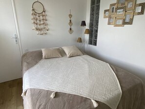 A bedroom with a bed, pillows, a dreamcatcher, a lamp, and framed pictures on the wall. - Renovated apartment in Nouméa, marina, parking (Canet-Plage)