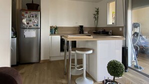 Ett modernt kök med en central köksö, barstolar, ett kylskåp med magneter och utsikt över en balkong.
