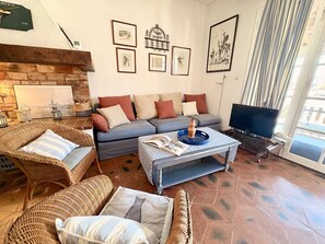 A living room with a sofa, two wicker chairs, a coffee table with books, a TV, and artwork on the walls. - Large fisherman's house near beach - 4 terraces, WiFi, parking (Port Grimaud)