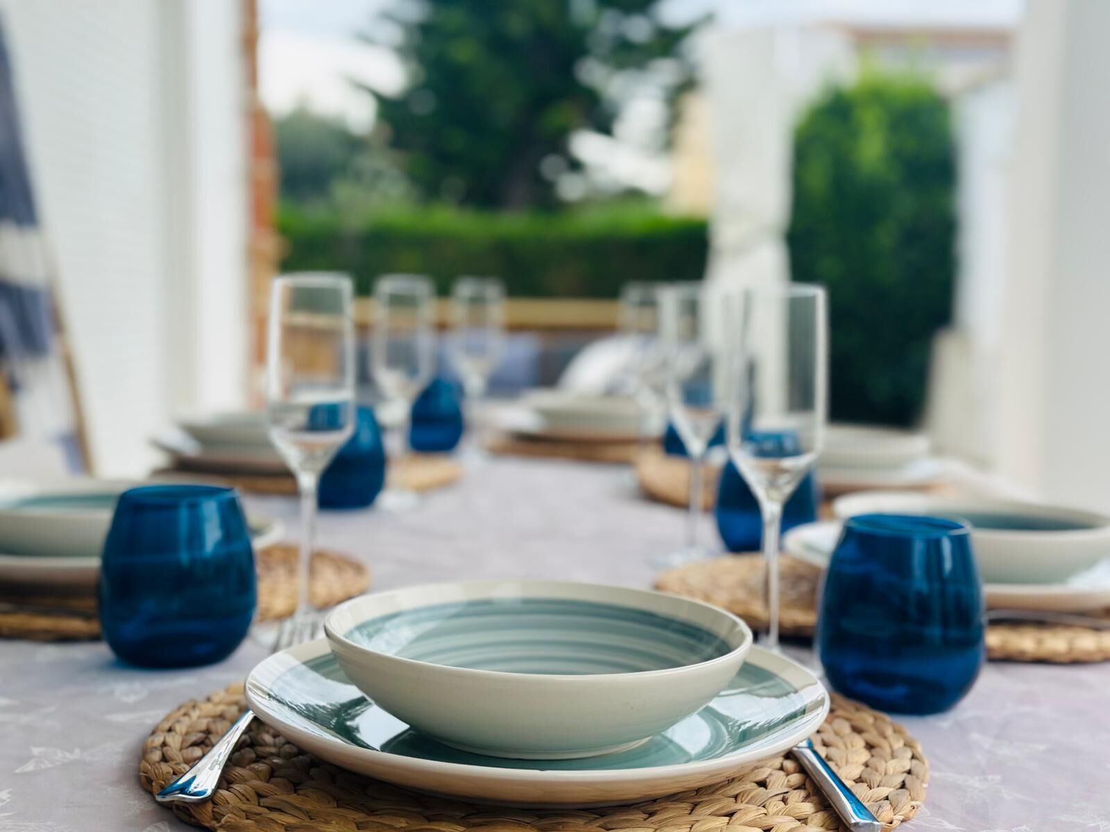 A table set with plates, glasses, and cutlery, arranged on woven placemats.