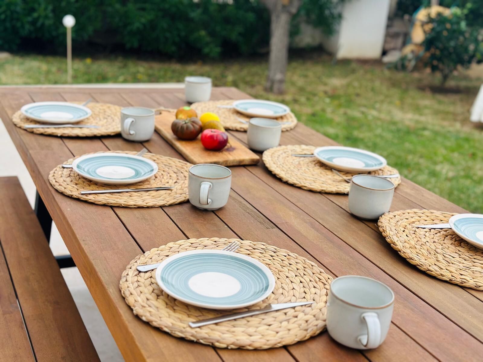 Un conjunto de mesa y sillas de picnic de madera con platos, cubiertos y tazas, rodeado de individuales tejidos.