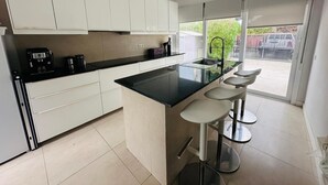 A modern kitchen with white cabinets, a black countertop, and a large island with bar stools. - Modern villa with private garden and pool. Ideal for families or small groups. (Las Palmeras)