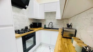 A compact kitchen with white cabinets, a black stove, a wooden countertop, a sink, and a toaster. - Near Hampden - Parking - Wifi - Sleeps 6 (Glasgow)