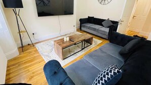 A living room with a grey sofa, a coffee table, a flat-screen TV, and a clock on the wall. - Near Hampden - Parking - Wifi - Sleeps 6 (Glasgow)