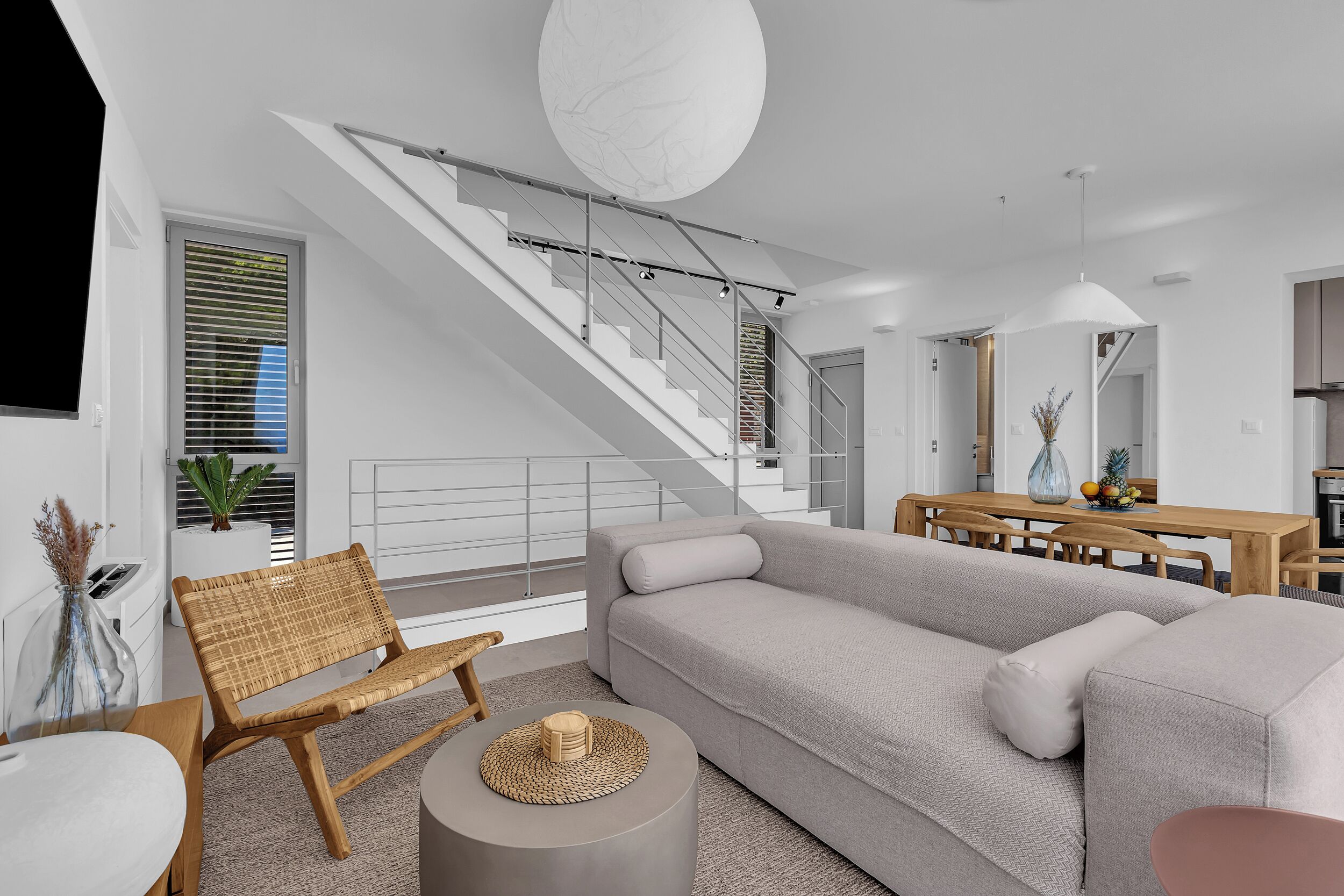 A modern living room with a grey sofa, a wooden chair, a round coffee table, and a staircase leading to another level.