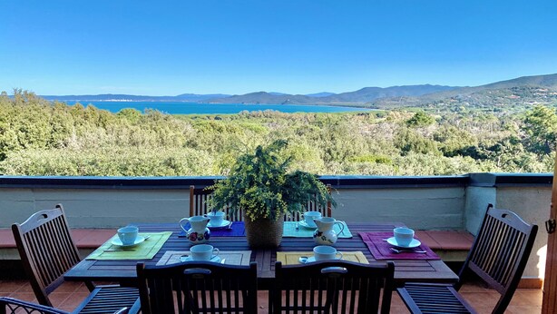 A terrace with a table set for tea, overlooking a scenic landscape with mountains and a body of water. - Stunning Panoramic Villa (Punta Ala)