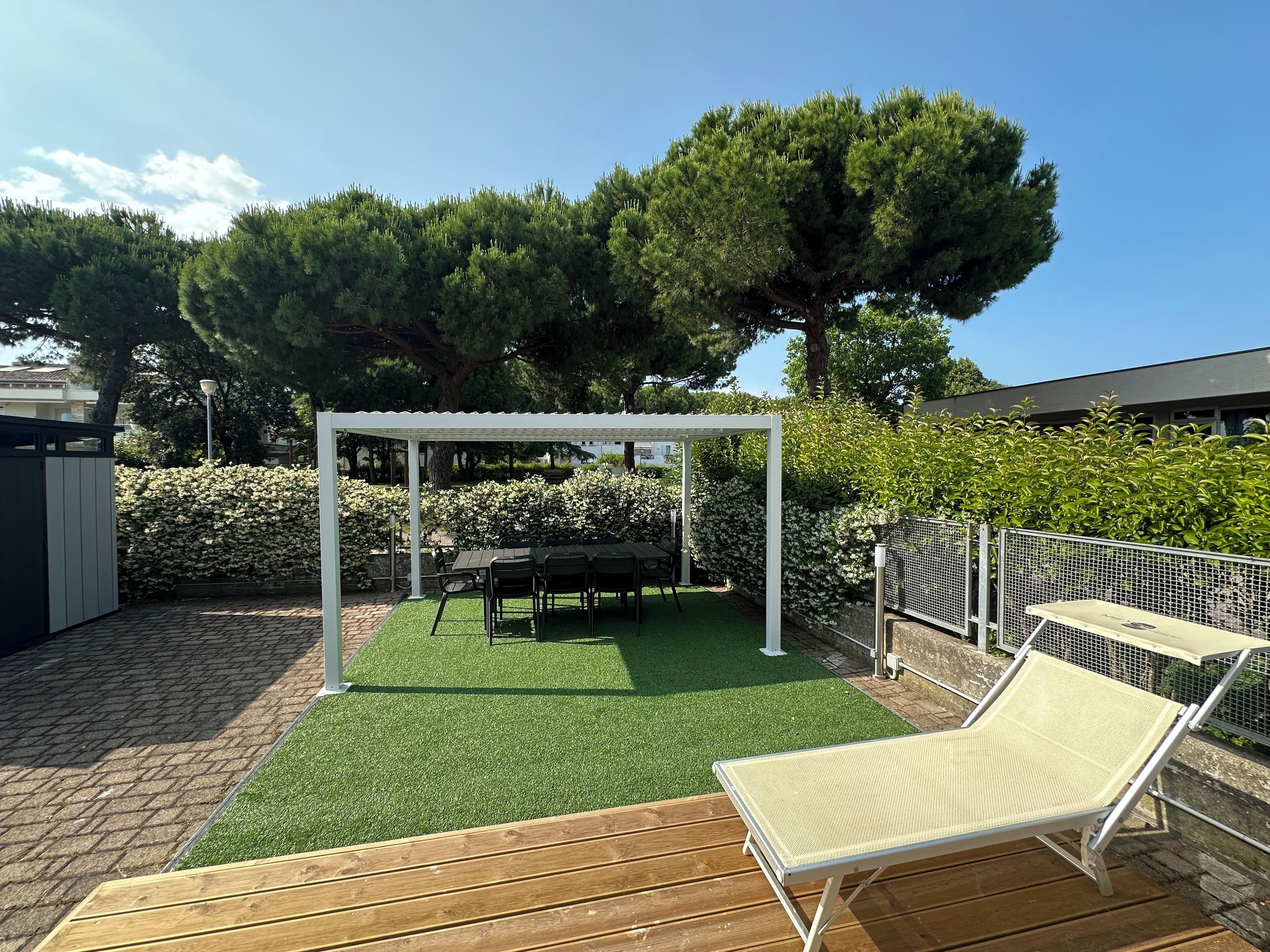 A covered patio area with a table and chairs, surrounded by greenery and a pergola.