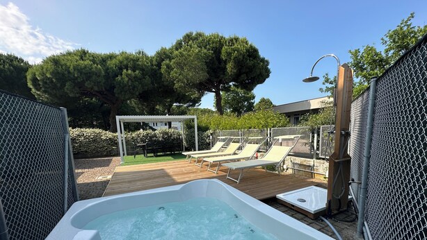 A hot tub with a wooden deck and lounge chairs, surrounded by a chain-link fence and a pergola. - Neptune Apartment Relax Privè Beach (Cervia)