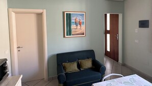 A room with a blue sofa, a painting of a beach scene, an air conditioning unit, and a door. - Neptune Apartment Relax Privè Beach (Cervia)