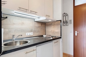 Una cocina moderna con un lavamanos de acero inoxidable, encimera negra y armarios blancos.