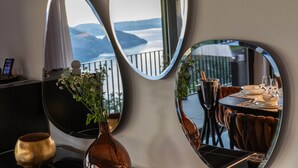 Un coin repas avec vue sur les montagnes, visible à travers une fenêtre, un miroir rond et un vase rempli de fleurs.