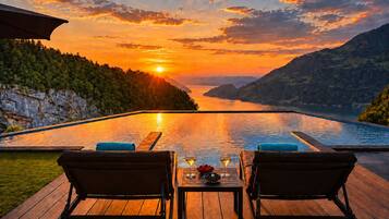 A sunset view from a poolside area with two lounge chairs and a table with drinks.