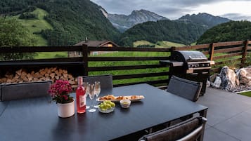 An outdoor dining area with a table set for a meal, a grill, and a scenic mountain view.