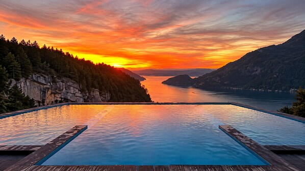 A infinity pool with a view of a sunset over a lake and mountains.