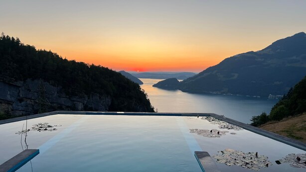 Une piscine à débordement paisible, offrant une vue dégagée sur un coucher de soleil se reflétant sur un paysage montagneux.