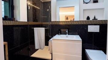 A modern bathroom with a glass shower enclosure, a white sink, and a marble-tiled wall with a decorative border.