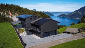 Un bâtiment moderne doté de panneaux solaires, d’un drapeau et offrant une vue sur un lac et des montagnes.